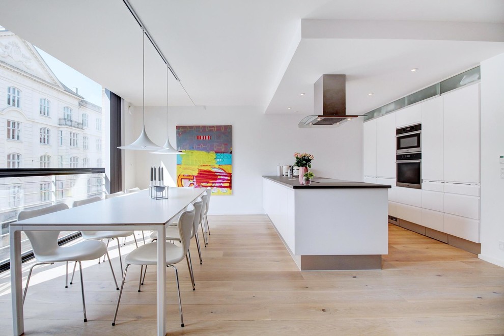This is an example of a modern open plan dining in Copenhagen with white walls, light hardwood floors and no fireplace.