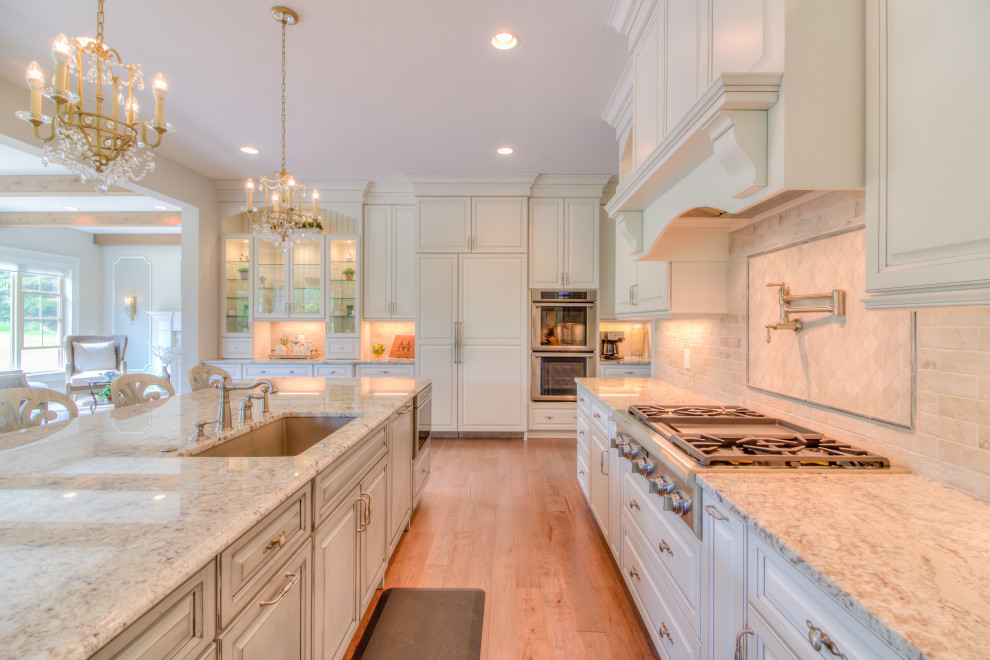 Design ideas for a large l-shaped eat-in kitchen in Cleveland with an undermount sink, beaded inset cabinets, white cabinets, granite benchtops, beige splashback, porcelain splashback, panelled appliances, light hardwood floors, with island, brown floor and beige benchtop.