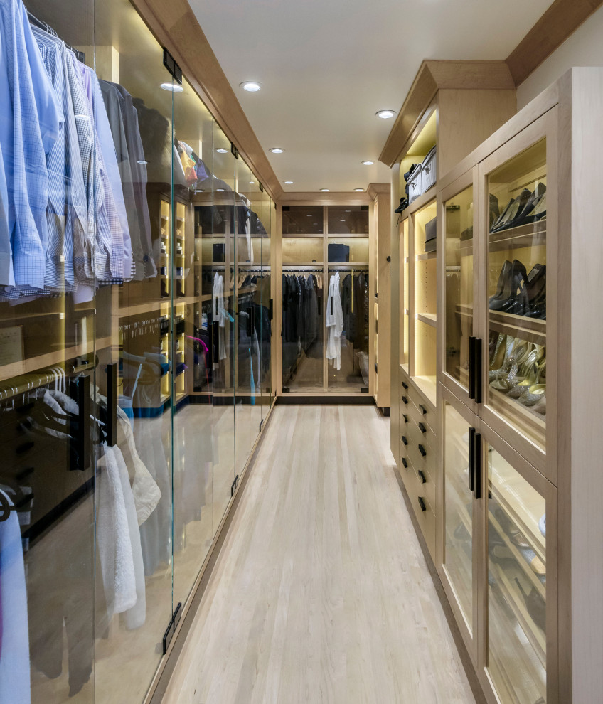 This is an example of a classic walk-in wardrobe in San Francisco with glass-front cabinets, light wood cabinets, light hardwood flooring and beige floors.