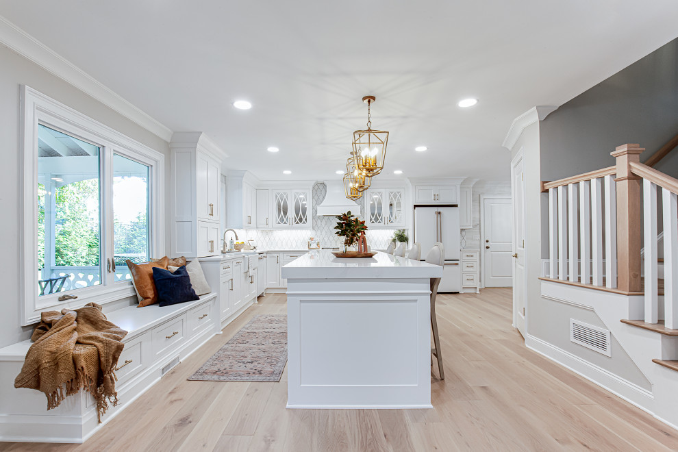 Design ideas for a large traditional l-shaped open plan kitchen in Atlanta with an undermount sink, beaded inset cabinets, white cabinets, quartz benchtops, white splashback, marble splashback, white appliances, light hardwood floors, with island, beige floor and white benchtop.