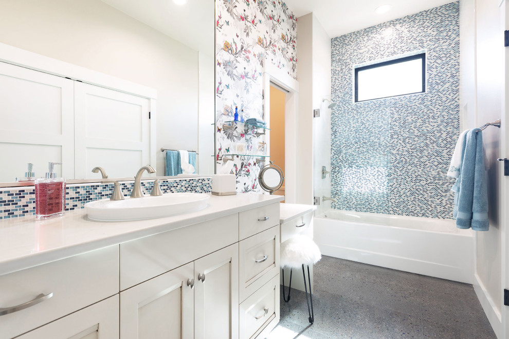 Photo of a transitional bathroom in Columbus with white cabinets, an alcove tub, a shower/bathtub combo, multi-coloured tile, concrete floors, a hinged shower door, white benchtops, a double vanity and a built-in vanity.