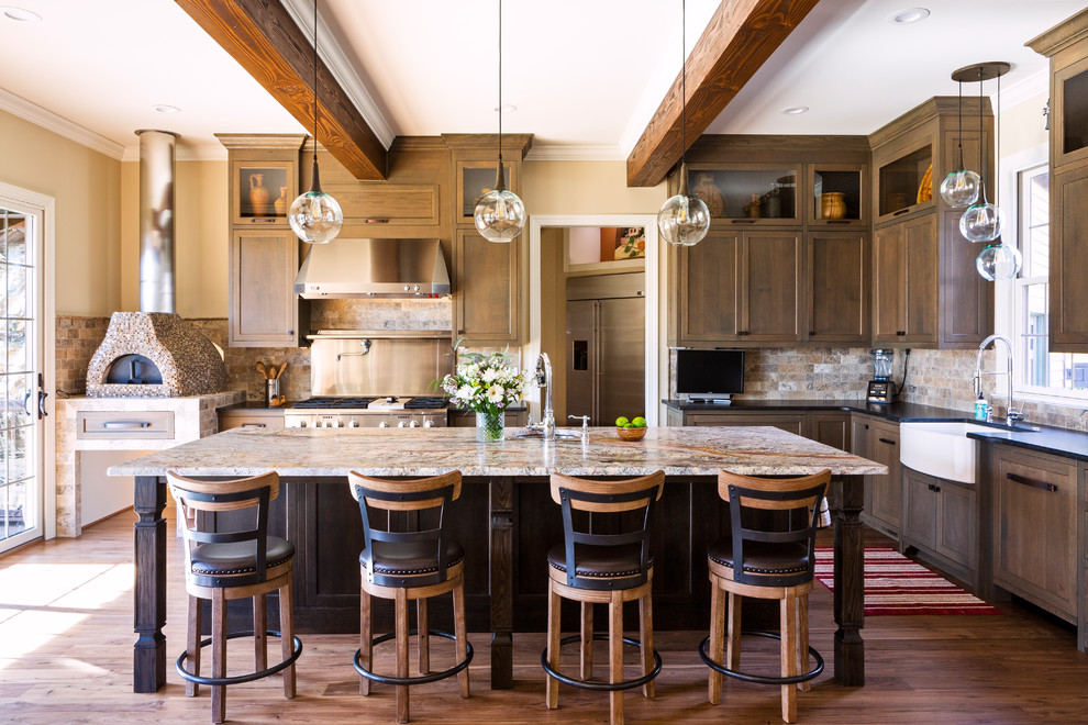 Country l-shaped kitchen in Charlotte with a farmhouse sink, granite benchtops, multi-coloured splashback, stone tile splashback, stainless steel appliances, medium hardwood floors, with island, brown floor, black benchtop, shaker cabinets and dark wood cabinets.