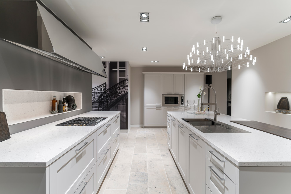 Large contemporary galley open plan kitchen in Cologne with an integrated sink, white cabinets, grey splashback, stainless steel appliances, with island, beige floor and white benchtop.