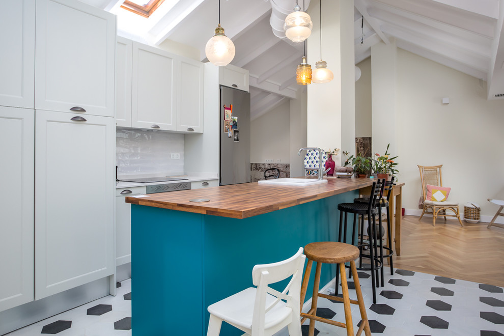 Inspiration for a mediterranean single-wall open plan kitchen in Madrid with shaker cabinets, with island, white splashback, stainless steel appliances, a drop-in sink, turquoise cabinets, wood benchtops, multi-coloured floor and brown benchtop.