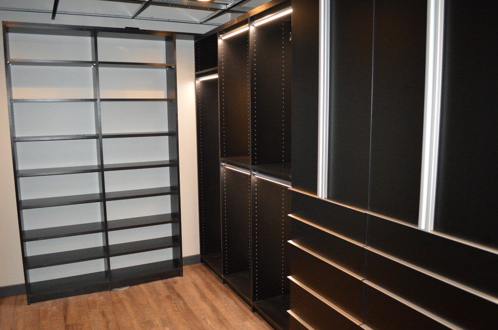 Large modern gender-neutral walk-in wardrobe in Cleveland with flat-panel cabinets, black cabinets and medium hardwood floors.