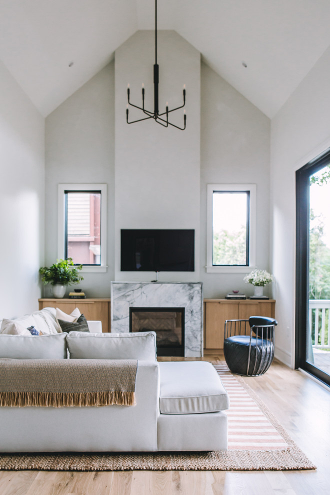 Design ideas for a scandinavian open plan living room in Raleigh with white walls, light hardwood flooring, a standard fireplace, a stone fireplace surround, a wall mounted tv, yellow floors and a vaulted ceiling.
