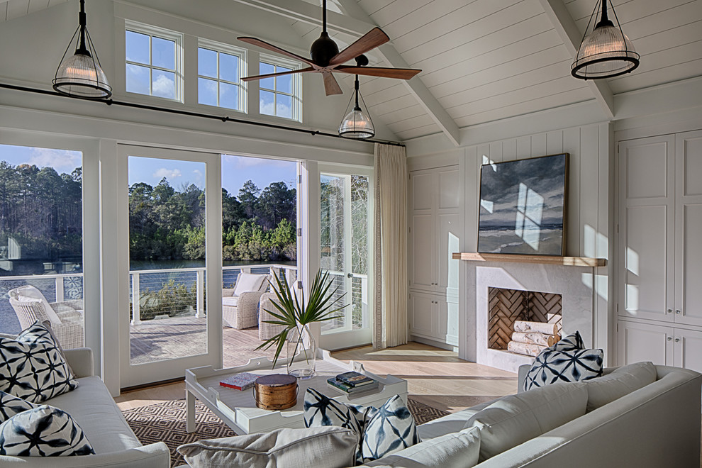Design ideas for a mid-sized country open concept family room in Charleston with white walls, light hardwood floors, a standard fireplace, a stone fireplace surround, a concealed tv and beige floor.