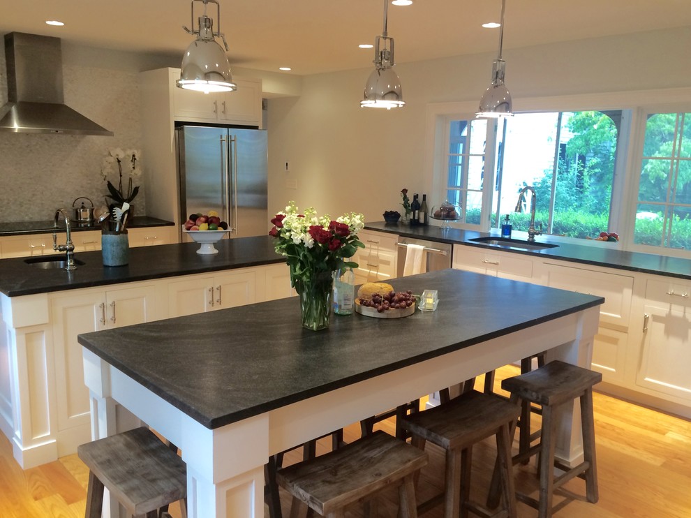 This is an example of a large country l-shaped eat-in kitchen in Portland Maine with shaker cabinets, white cabinets, soapstone benchtops, grey splashback, marble splashback, stainless steel appliances, medium hardwood floors, multiple islands and beige floor.