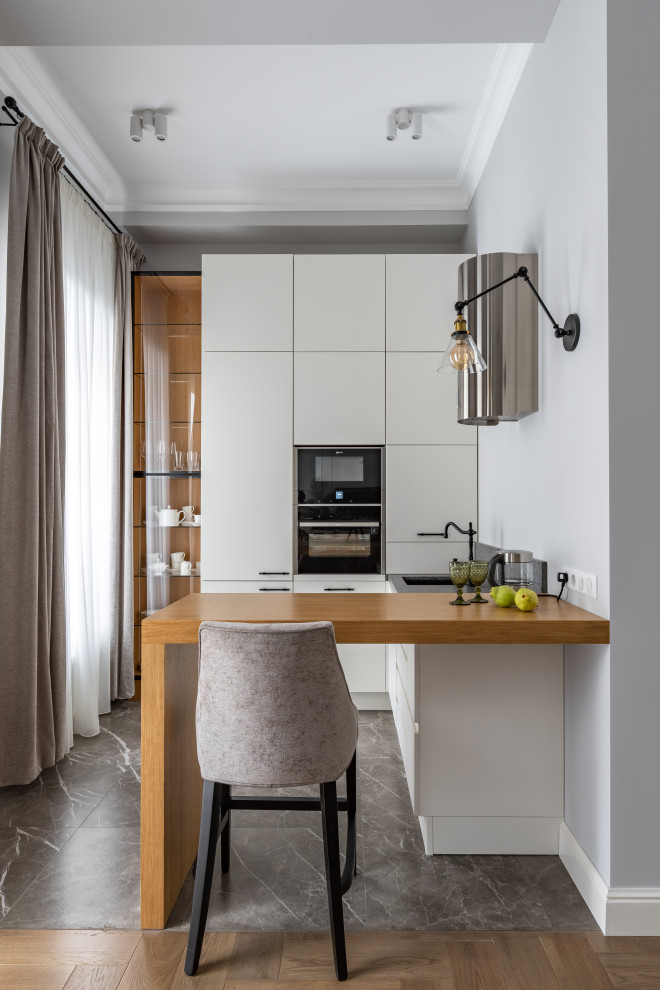 Photo of a small traditional u-shaped open plan kitchen in Moscow with a single-bowl sink, flat-panel cabinets, white cabinets, wood worktops, black splashback, engineered quartz splashback, black appliances, porcelain flooring, a breakfast bar, grey floors, yellow worktops and exposed beams.