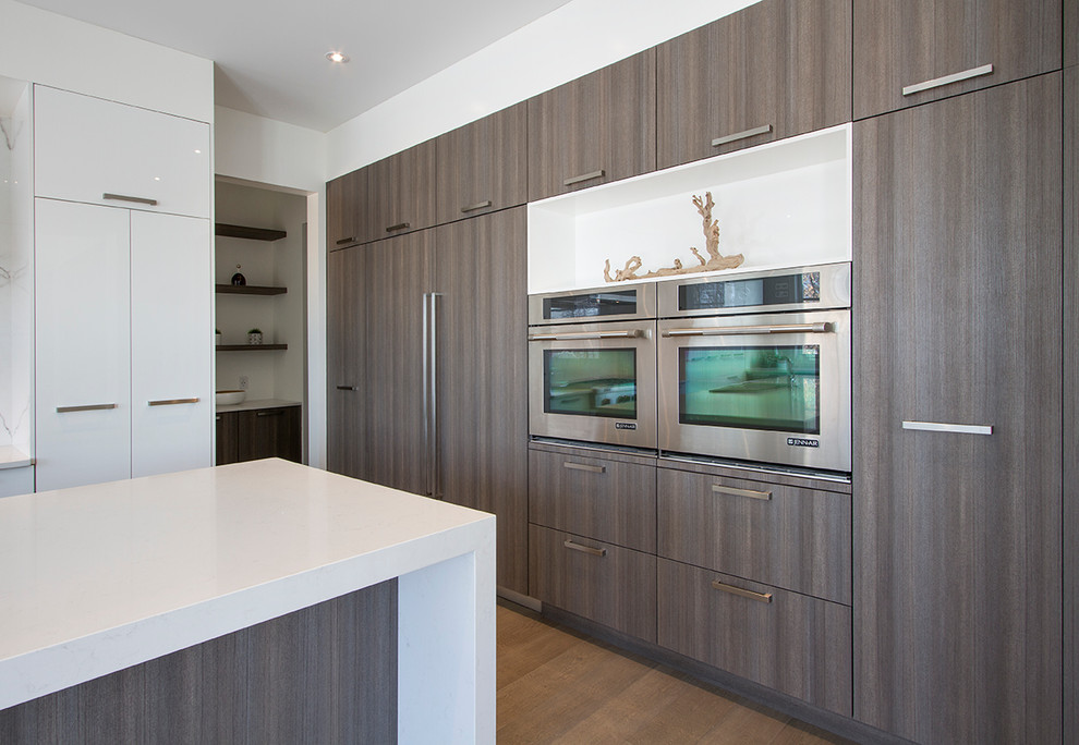 This is an example of an expansive contemporary u-shaped eat-in kitchen in Calgary with an undermount sink, flat-panel cabinets, grey cabinets, quartz benchtops, white splashback, panelled appliances, light hardwood floors, with island and white benchtop.