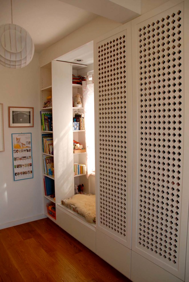 Photo of a modern gender-neutral kids' bedroom for kids 4-10 years old in New York with white walls and medium hardwood floors.