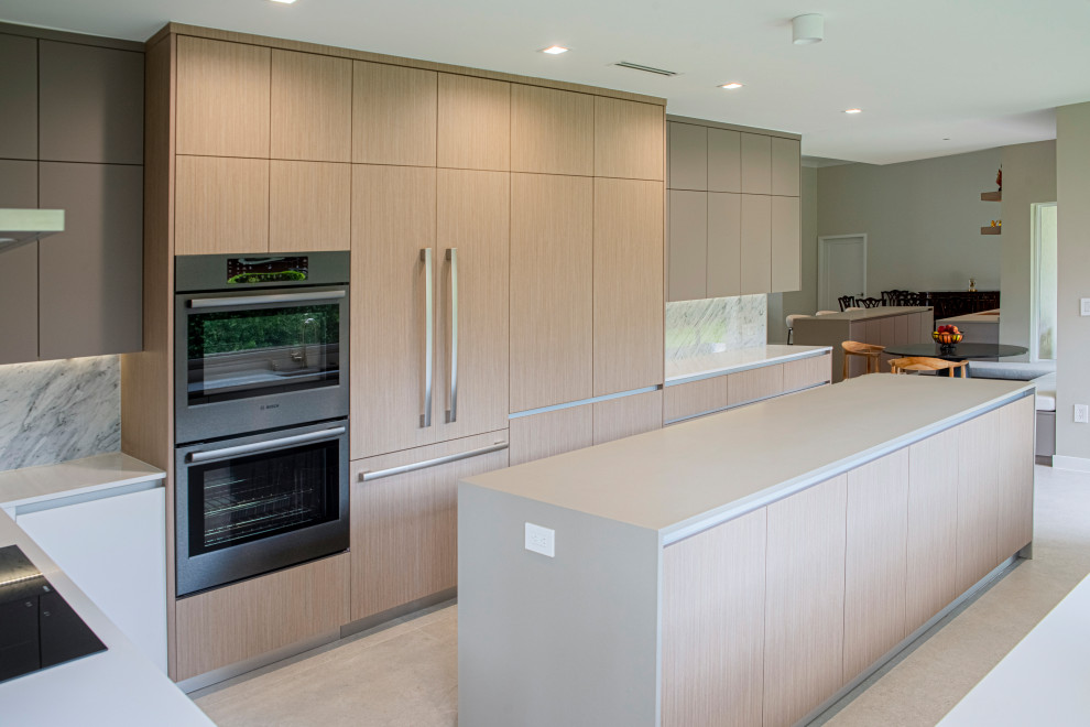 Photo of a large modern u-shaped kitchen/diner in Miami with a submerged sink, flat-panel cabinets, light wood cabinets, engineered stone countertops, white splashback, marble splashback, integrated appliances, porcelain flooring, an island, beige floors and white worktops.