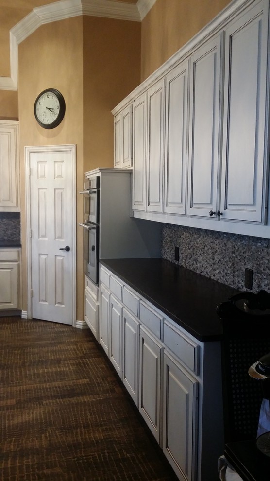 Example of a large transitional brown floor open concept kitchen design in Dallas with an undermount sink, raised-panel cabinets, white cabinets, granite countertops, gray backsplash, stone tile backsplash, stainless steel appliances and an island