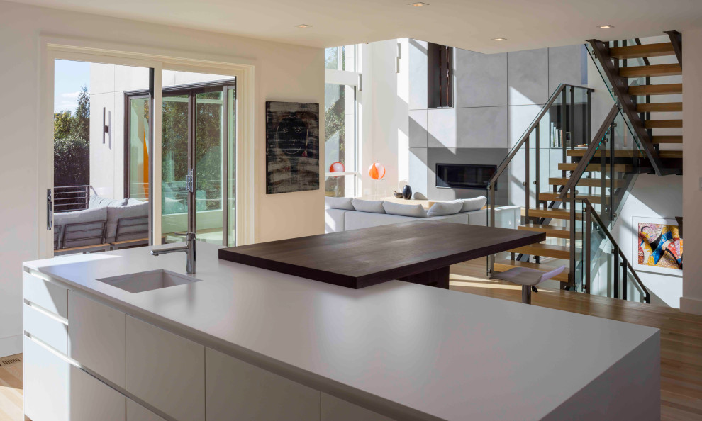 This is an example of a mid-sized modern eat-in kitchen in DC Metro with a single-bowl sink, flat-panel cabinets, white cabinets, light hardwood floors, with island, beige floor, grey splashback and white benchtop.