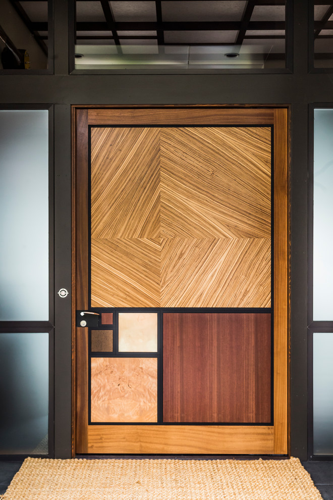 Design ideas for a mid-sized midcentury front door in Seattle with black walls, limestone floors, a pivot front door, a brown front door and black floor.