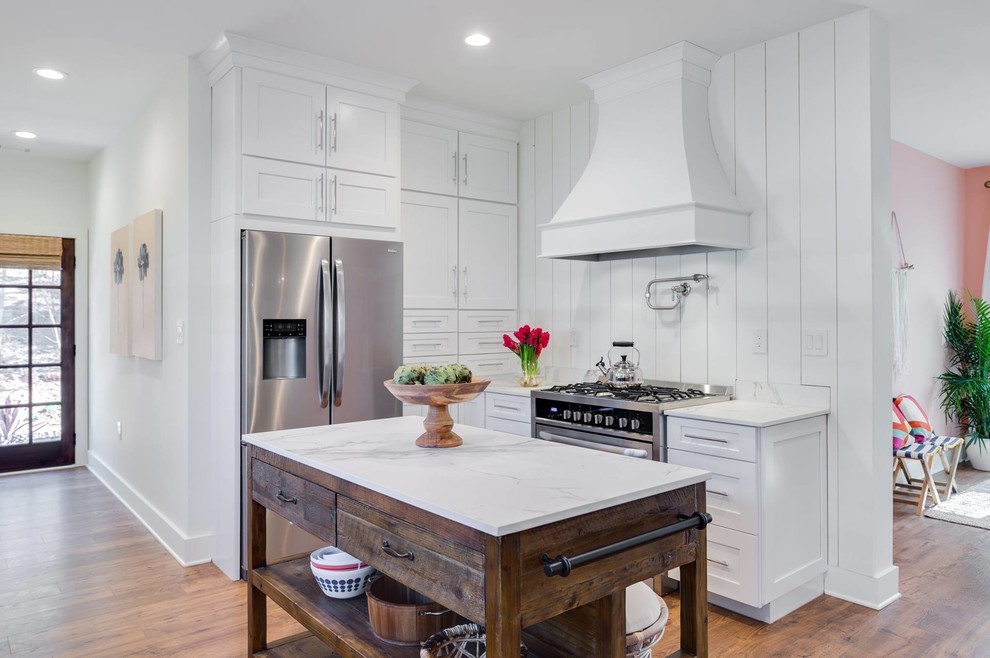 This is an example of a beach style kitchen in Other with shaker cabinets, white cabinets, white splashback, stainless steel appliances, medium hardwood floors, with island and white benchtop.