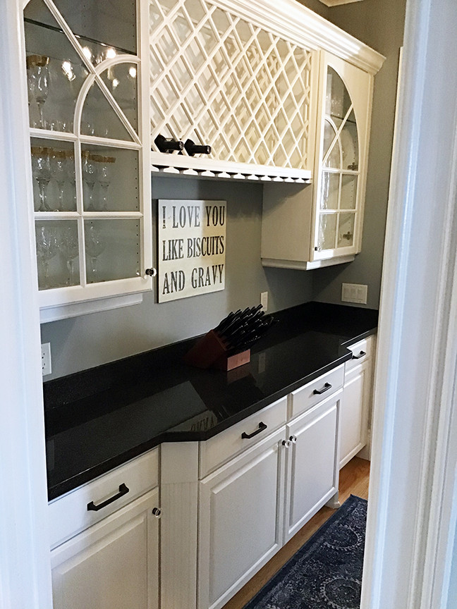 This is an example of a small transitional u-shaped wet bar in Orlando with an undermount sink, raised-panel cabinets, white cabinets, granite benchtops, blue splashback, medium hardwood floors, brown floor and black benchtop.