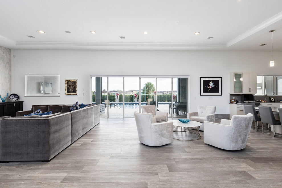 This is an example of a mid-sized contemporary formal open concept living room in Orlando with white walls, light hardwood floors, no fireplace, a wall-mounted tv and grey floor.