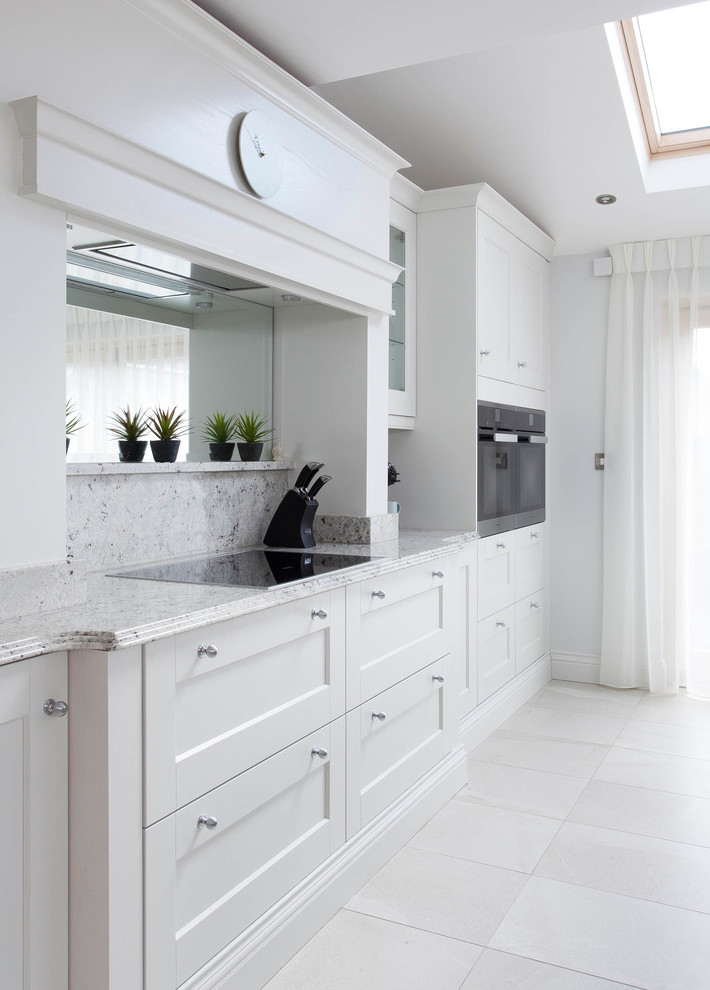 Large traditional l-shaped open plan kitchen in Dublin with an integrated sink, shaker cabinets, blue cabinets, granite worktops, multi-coloured splashback, stone slab splashback, black appliances, ceramic flooring and an island.