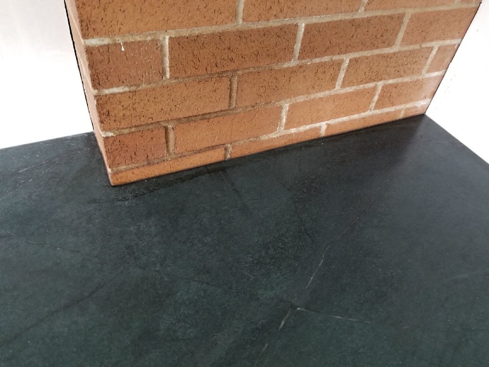 Example of a minimalist u-shaped ceramic tile and beige floor eat-in kitchen design with an undermount sink, flat-panel cabinets, white cabinets, soapstone countertops, stainless steel appliances, a peninsula and black countertops