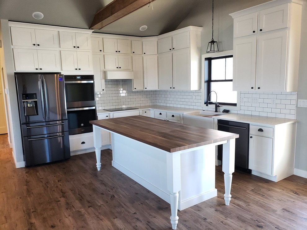 Mid-sized country l-shaped eat-in kitchen in Minneapolis with a farmhouse sink, flat-panel cabinets, white cabinets, quartz benchtops, white splashback, subway tile splashback, stainless steel appliances, vinyl floors, with island, grey floor and white benchtop.