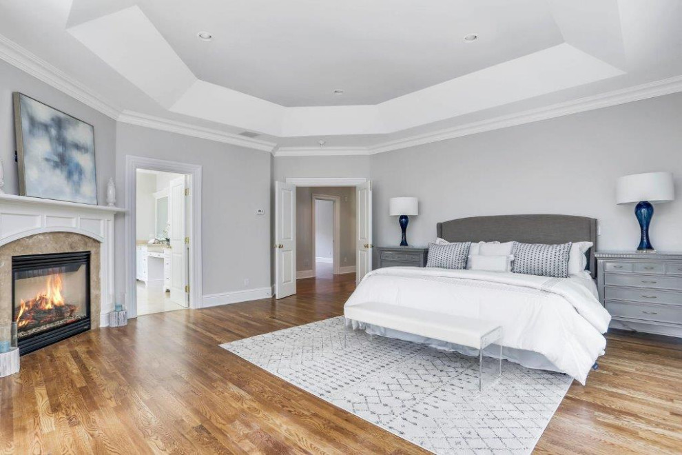 Inspiration for a large transitional master bedroom in New York with grey walls, medium hardwood floors, a standard fireplace, a stone fireplace surround and recessed.