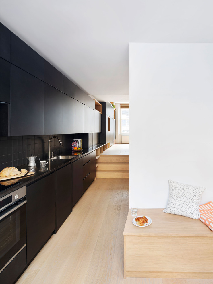 Inspiration for a large contemporary single-wall beige floor kitchen remodel in London with an undermount sink, flat-panel cabinets, black cabinets, black backsplash, porcelain backsplash, stainless steel appliances, no island and black countertops