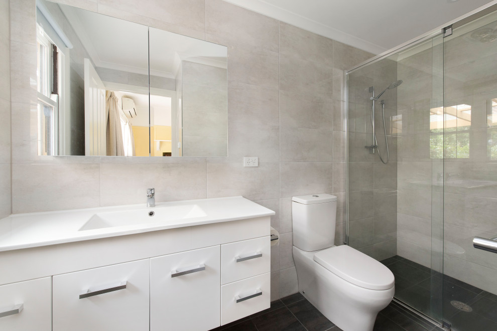 This is an example of a mid-sized traditional master bathroom in Canberra - Queanbeyan with flat-panel cabinets, white cabinets, a double shower, a one-piece toilet, gray tile, ceramic tile, grey walls, ceramic floors, an integrated sink, laminate benchtops, grey floor, a hinged shower door, white benchtops, a single vanity and a floating vanity.