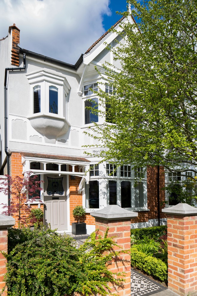 Mid-sized traditional two-storey brick white house exterior in London with a gable roof and a tile roof.