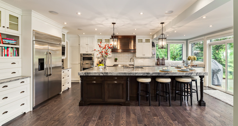 Mid-sized transitional l-shaped medium tone wood floor and brown floor enclosed kitchen photo in Calgary with an undermount sink, shaker cabinets, white cabinets, granite countertops, white backsplash, ceramic backsplash, stainless steel appliances and an island