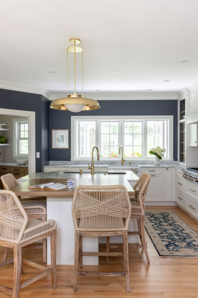 Photo of a mid-sized traditional l-shaped eat-in kitchen in Portland Maine with a farmhouse sink, flat-panel cabinets, white cabinets, marble benchtops, white splashback, ceramic splashback, stainless steel appliances, light hardwood floors, with island and blue benchtop.