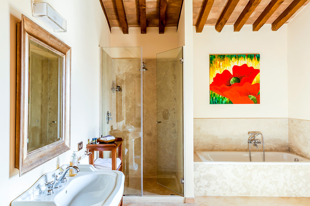 Mediterranean master bathroom in Palma de Mallorca with open cabinets, medium wood cabinets, a drop-in tub, an alcove shower, travertine, beige walls, terra-cotta floors, a pedestal sink, beige floor and a hinged shower door.