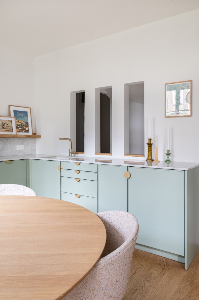 Country open plan kitchen in Paris with an undermount sink, beaded inset cabinets, green cabinets, marble benchtops, grey splashback, marble splashback, white appliances and grey benchtop.