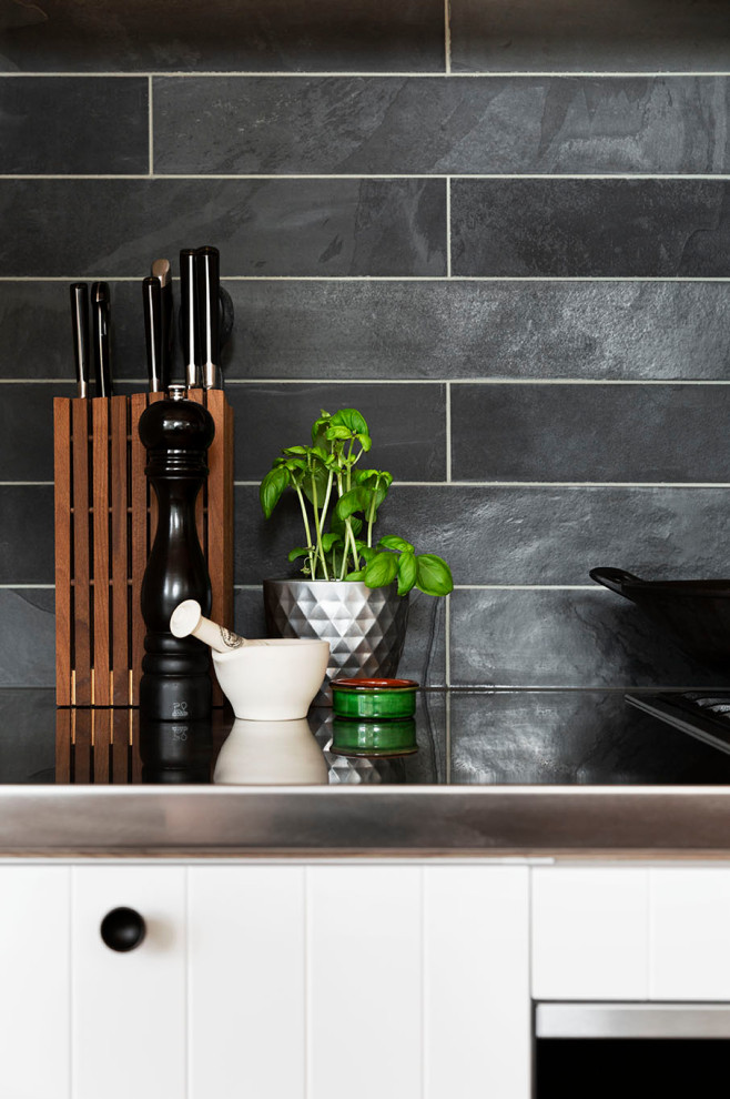 Foto på ett stort vintage svart linjärt kök med öppen planlösning, med en nedsänkt diskho, släta luckor, vita skåp, svart stänkskydd, stänkskydd i skiffer, rostfria vitvaror, ljust trägolv, en köksö och beiget golv