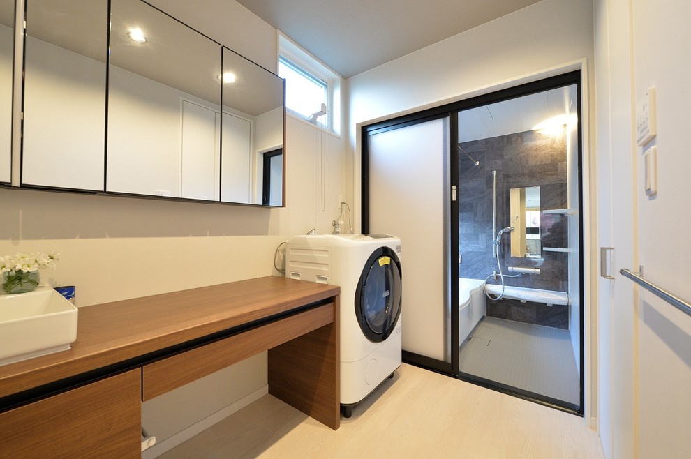 Photo of a modern laundry room in Other with flat-panel cabinets, medium wood cabinets, wood benchtops, white walls, painted wood floors, beige floor, brown benchtop and an integrated washer and dryer.