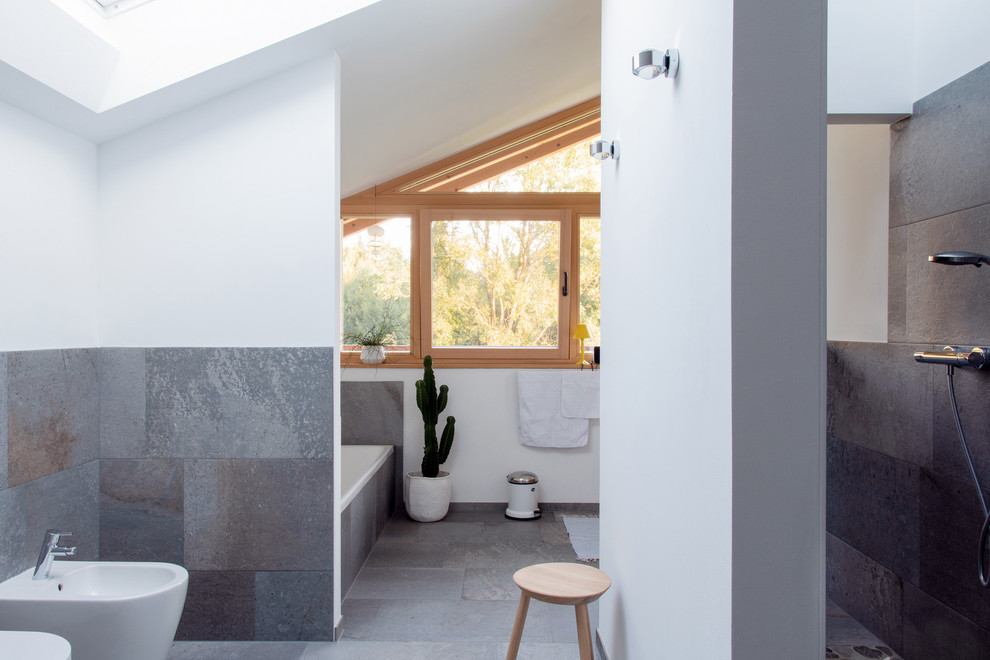 Photo of a scandinavian 3/4 bathroom in Munich with a drop-in tub, an open shower, a bidet, gray tile, white walls, grey floor and an open shower.