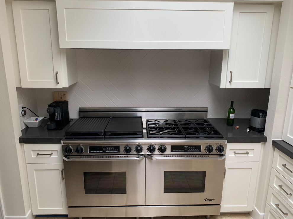 Kitchen - large transitional travertine floor and beige floor kitchen idea in Orange County with a single-bowl sink, shaker cabinets, white cabinets, quartzite countertops, white backsplash, ceramic backsplash, stainless steel appliances, an island and black countertops