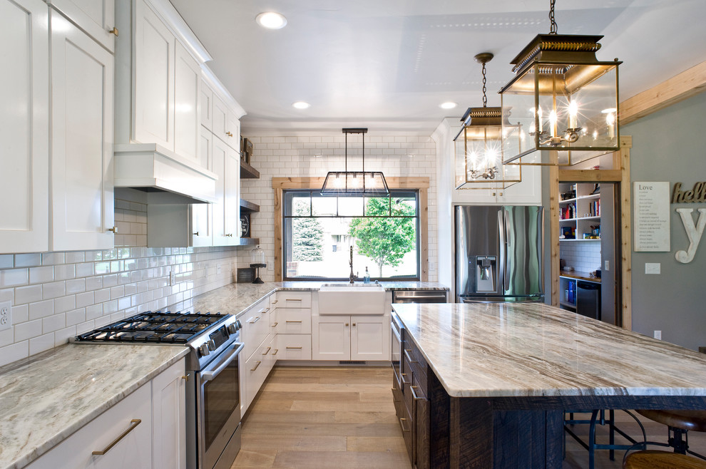 Mid-sized transitional u-shaped light wood floor and brown floor eat-in kitchen photo with a farmhouse sink, raised-panel cabinets, white cabinets, granite countertops, white backsplash, subway tile backsplash, stainless steel appliances and an island