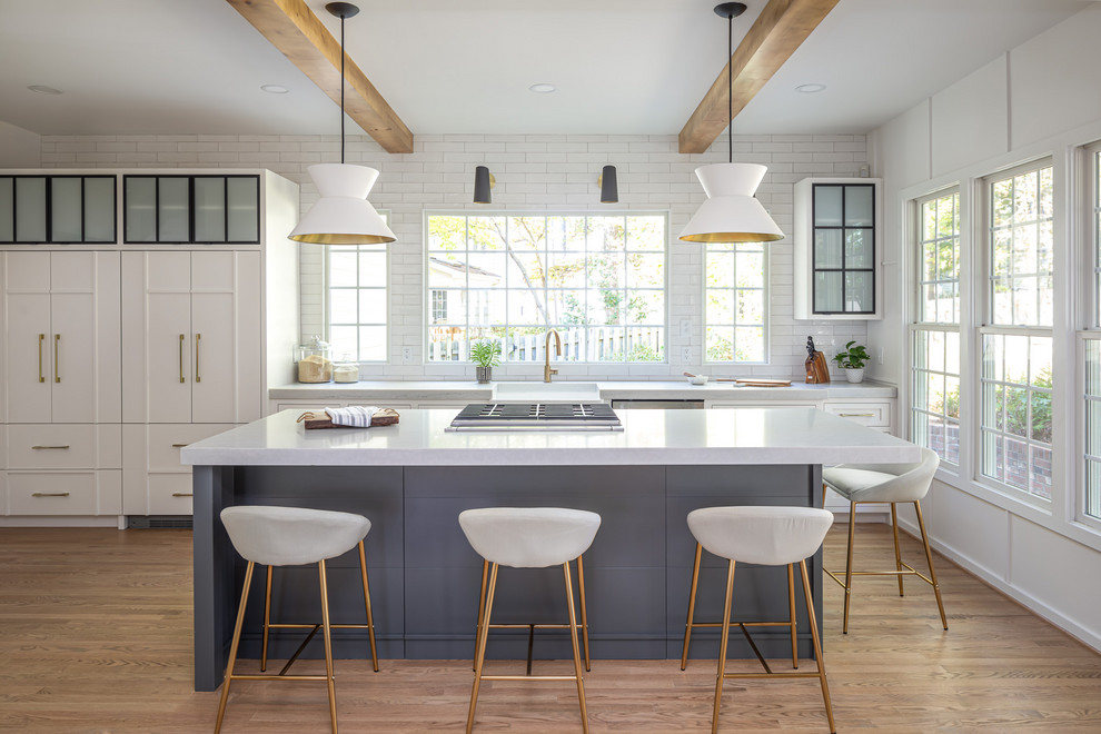 Inspiration for a mid-sized country kitchen in Raleigh with a farmhouse sink, white cabinets, quartzite benchtops, white splashback, subway tile splashback, panelled appliances, light hardwood floors, with island, white benchtop, beige floor and glass-front cabinets.