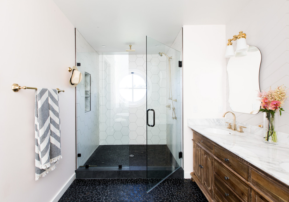 Photo of a transitional bathroom in Sacramento with raised-panel cabinets, brown cabinets, an alcove shower, white tile, white walls, pebble tile floors, an undermount sink, black floor and a hinged shower door.