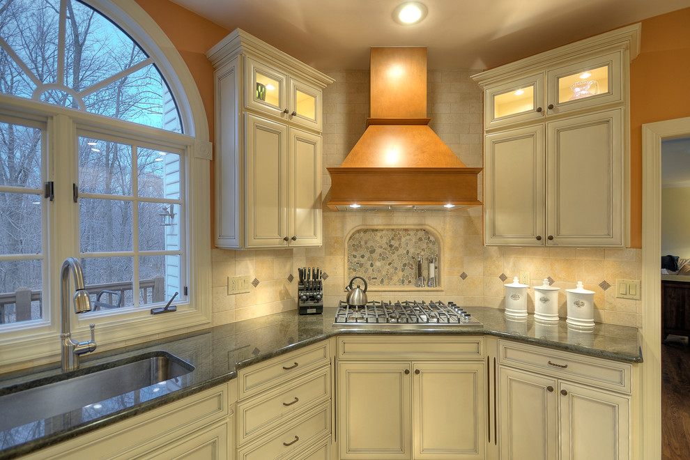 Photo of a large traditional l-shaped eat-in kitchen in Philadelphia with an undermount sink, raised-panel cabinets, white cabinets, granite benchtops, beige splashback, porcelain splashback, stainless steel appliances, with island and dark hardwood floors.