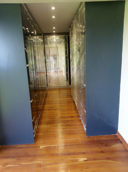 Foto di una piccola cabina armadio unisex contemporanea con ante di vetro, ante in legno bruno, pavimento in laminato, pavimento marrone e travi a vista