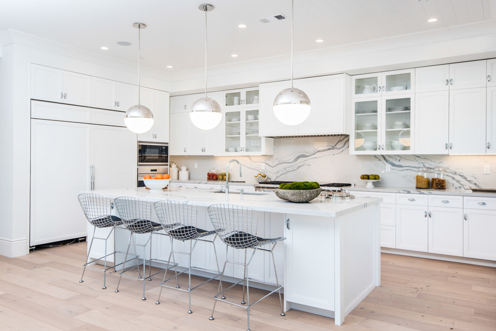 This is an example of a transitional kitchen in Los Angeles with an undermount sink, glass-front cabinets, white cabinets, white splashback, panelled appliances, light hardwood floors and with island.