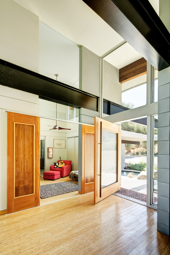This is an example of a large contemporary foyer in Other with a pivot front door, a medium wood front door, beige walls and light hardwood floors.