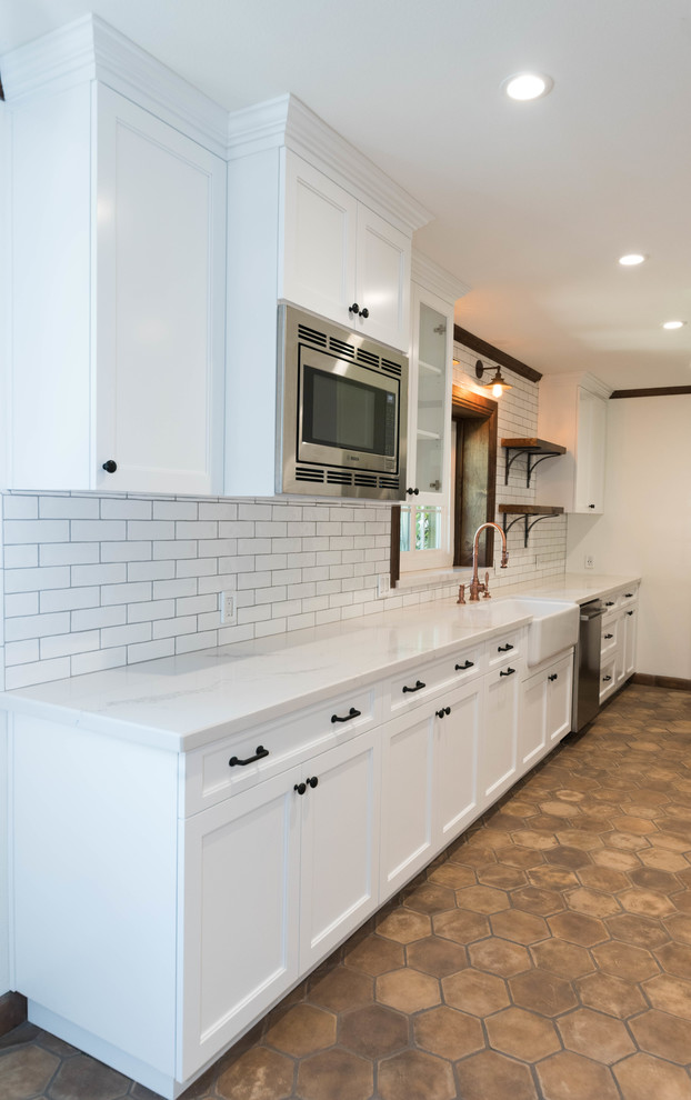 Photo of a mid-sized industrial u-shaped eat-in kitchen in San Francisco with a farmhouse sink, flat-panel cabinets, white cabinets, quartzite benchtops, ceramic splashback, stainless steel appliances, terra-cotta floors and brown floor.
