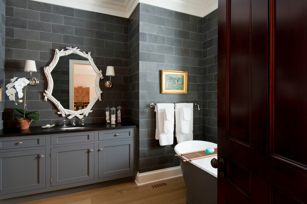 This is an example of a traditional bathroom in New York with an undermount sink, recessed-panel cabinets, grey cabinets, a freestanding tub, gray tile and medium hardwood floors.