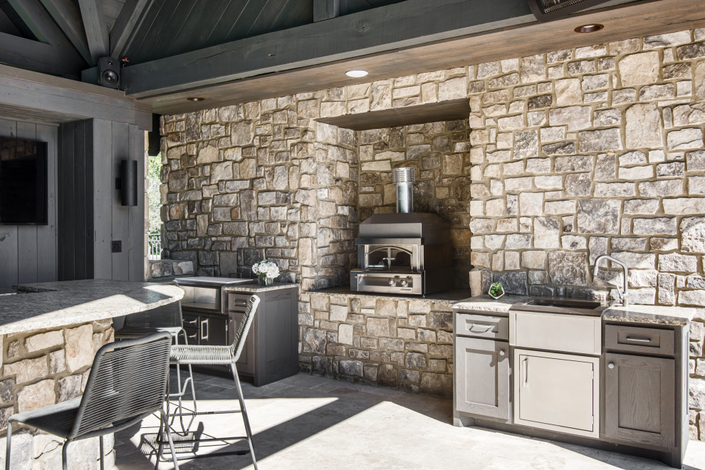 На фото: огромная веранда на заднем дворе в стиле неоклассика (современная классика) с летней кухней, покрытием из каменной брусчатки и навесом