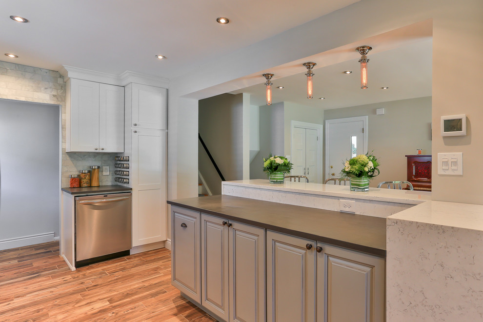 Photo of a mid-sized transitional single-wall eat-in kitchen in Toronto with a farmhouse sink, shaker cabinets, white cabinets, grey splashback, stainless steel appliances, with island, quartzite benchtops, stone tile splashback and light hardwood floors.