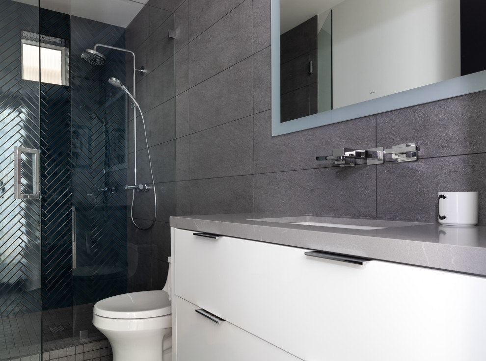 Mid-sized contemporary 3/4 bathroom in Orange County with flat-panel cabinets, white cabinets, an open shower, a one-piece toilet, white tile, porcelain tile, white walls, porcelain floors, an undermount sink, engineered quartz benchtops, grey floor, a hinged shower door and grey benchtops.
