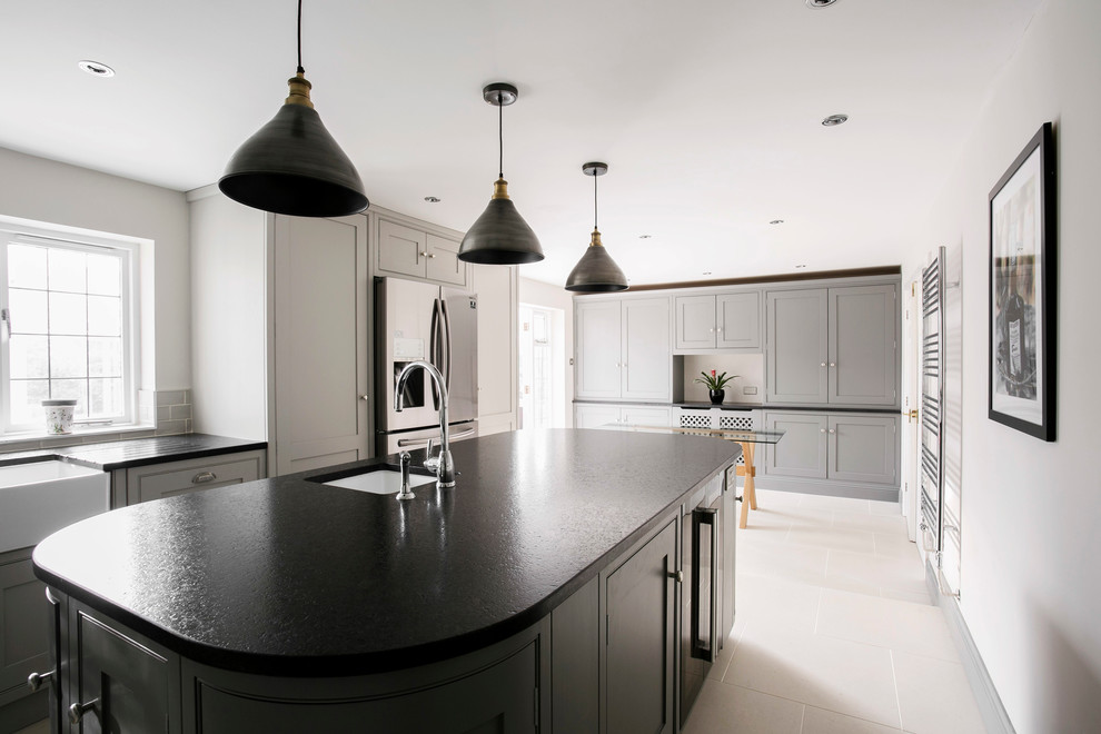 Mid-sized contemporary u-shaped eat-in kitchen in Kent with a farmhouse sink, shaker cabinets, grey cabinets, granite benchtops, ceramic floors, with island, white splashback, subway tile splashback, panelled appliances, white floor and black benchtop.